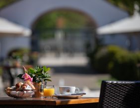 gedeckter Frühstückstisch im Innenhof mit Blick zum qweißen Eingangstor des Hotel Schloss Reinach